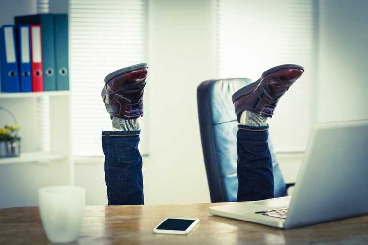 Businessman upside down with feet in the air at his desk.