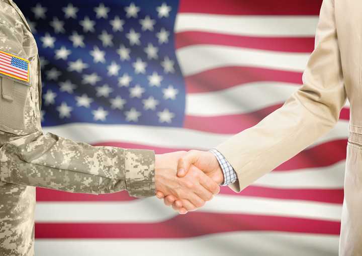 American solider in uniform shaking hands with another person in front of an American flag